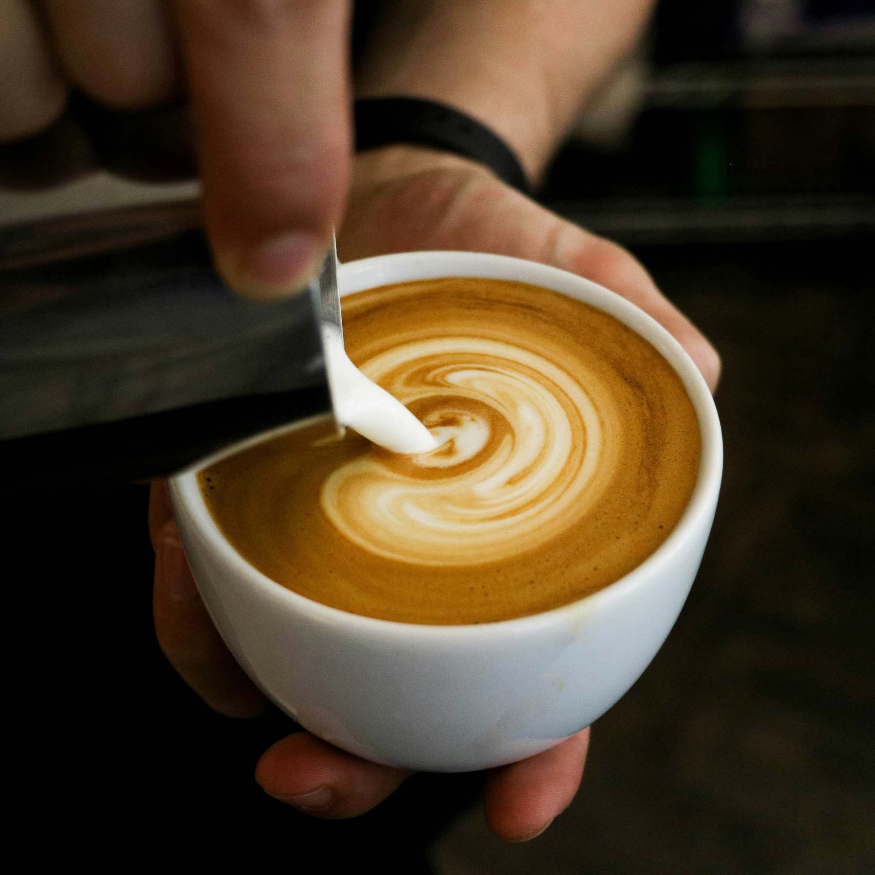A barista pouring latte art into a cup at a local coffee shop